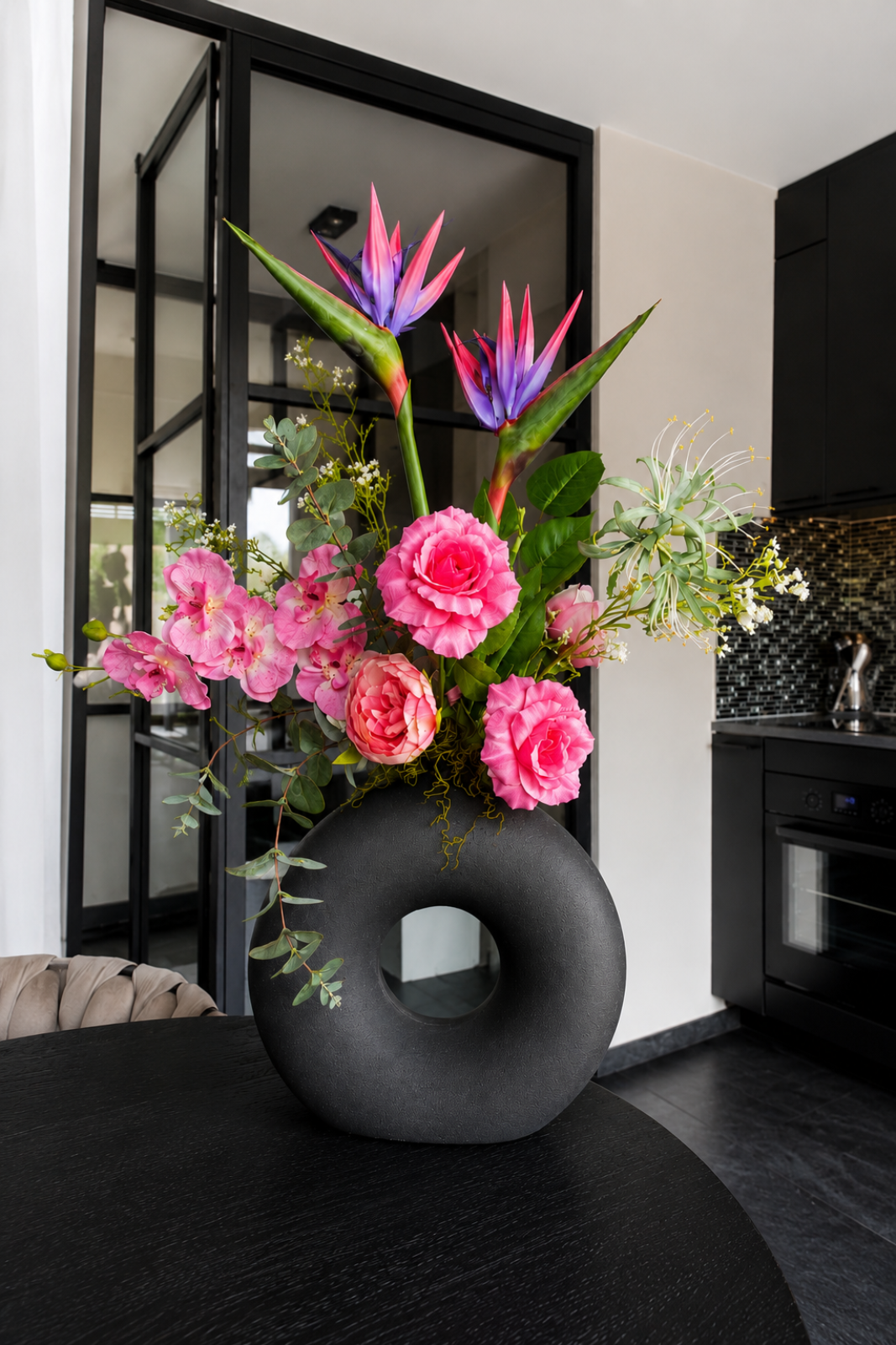 Luxe zijdebloemstuk met roze rozen, strelitzia bloemen en eucalyptus in moderne zwarte designvaas